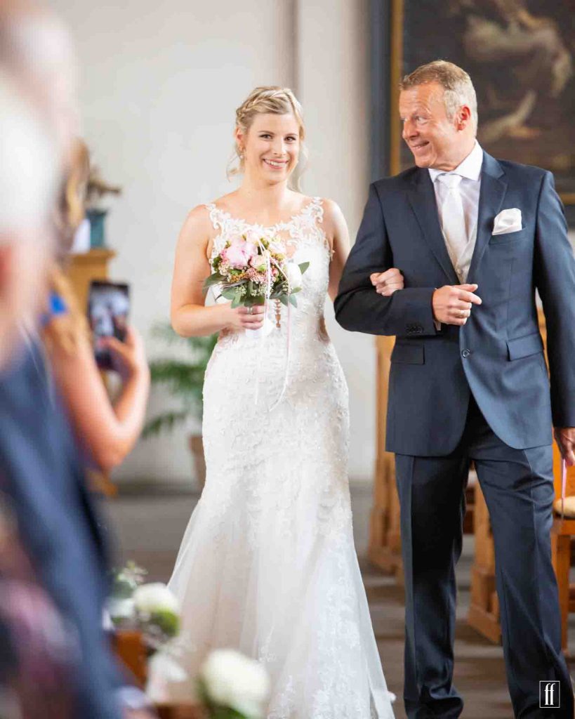 Porträt einer Braut, die von ihrem Vater zum Altar geführt wird.