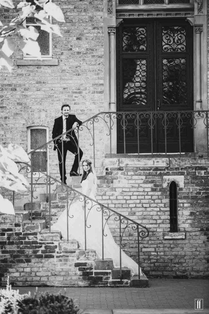 Braut und Bräutigam stehen auf einer Treppe und schauen lächelnd in die Kamera