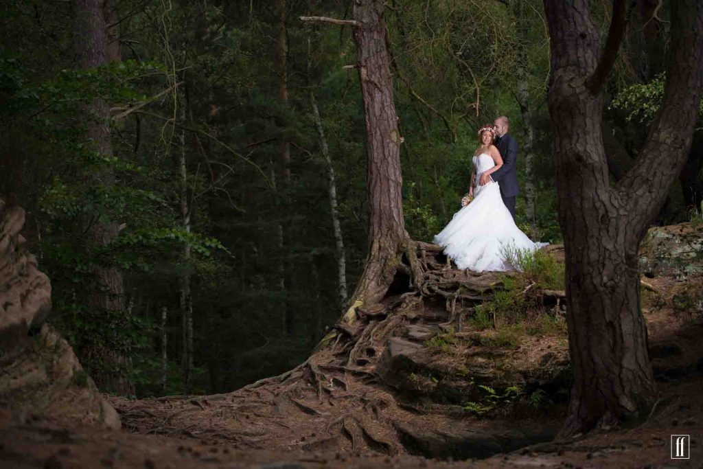 Brautpaar steht in einem schönen Wald und werden von den Bäumen ästhetisch eingerahmt.