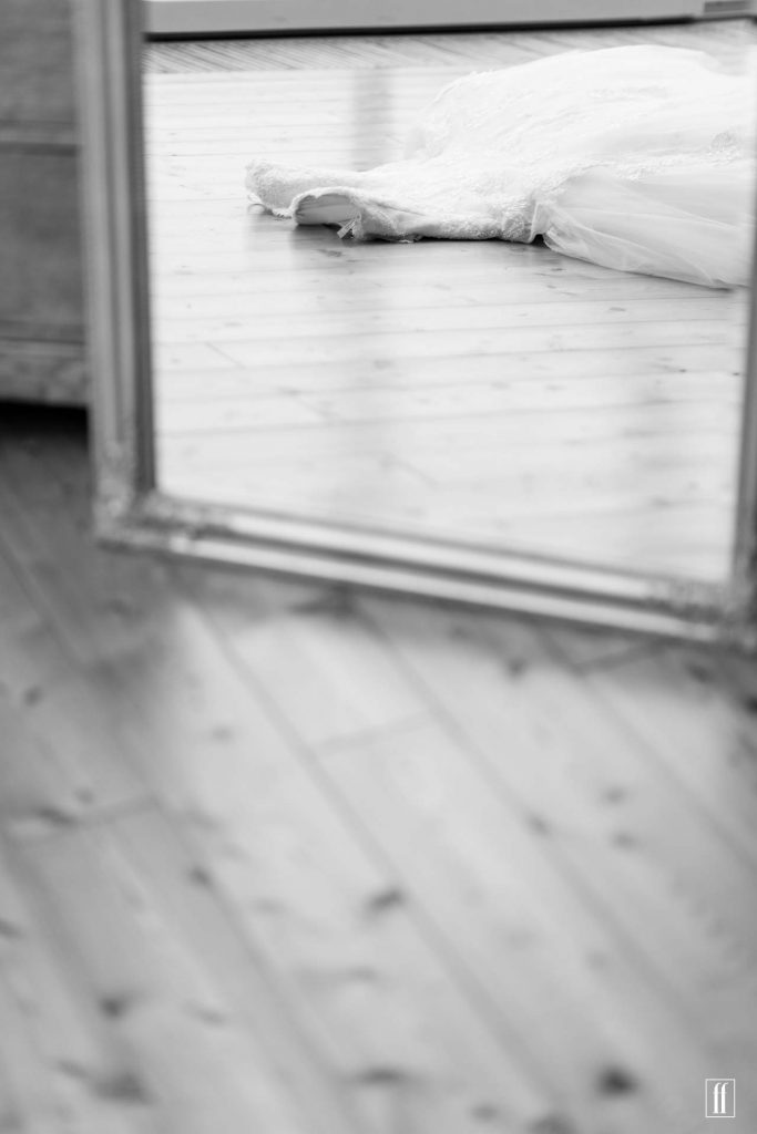 Ein Hochzeitskleid liegt beim getting ready der Braut auf dem Holzboden und wird durch einen Spiegel gesehen.