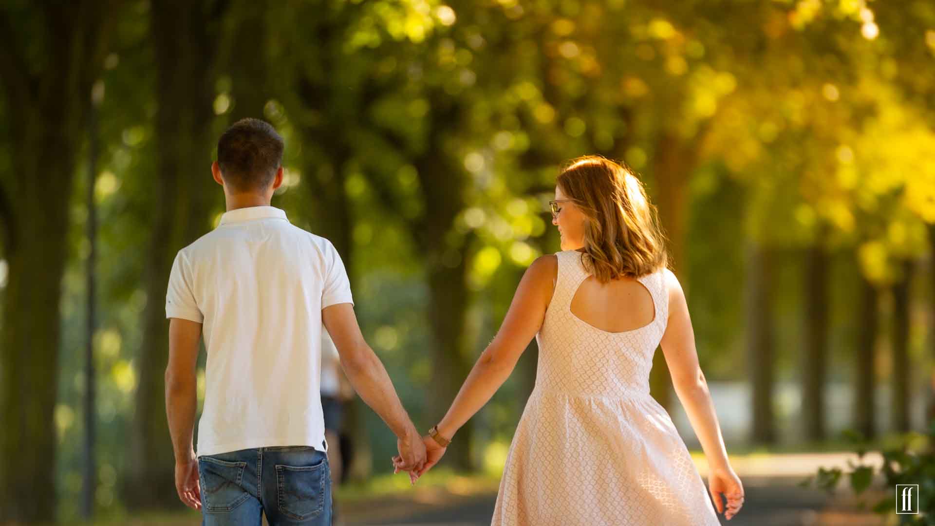 Ein Pärchen geht händchenhaltend eine sonnige Allee entlang